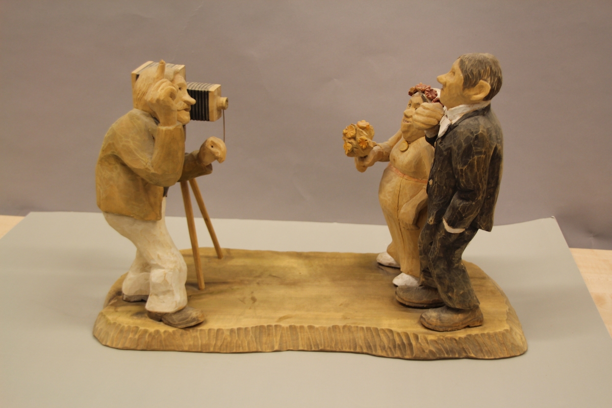 Skulptur som syner Arne Aas som tek bilete av eit brudepar. Skulpturen er skoren i tre.Tekst under:"Bjarne Walle fra Bamle laget denne gruppa på bestilling i fra fotografen Arne Aas i 1984" "Motiv: Arne Aas fotograferer brudepar". Bokstavane BW skore inn under skulpturen.