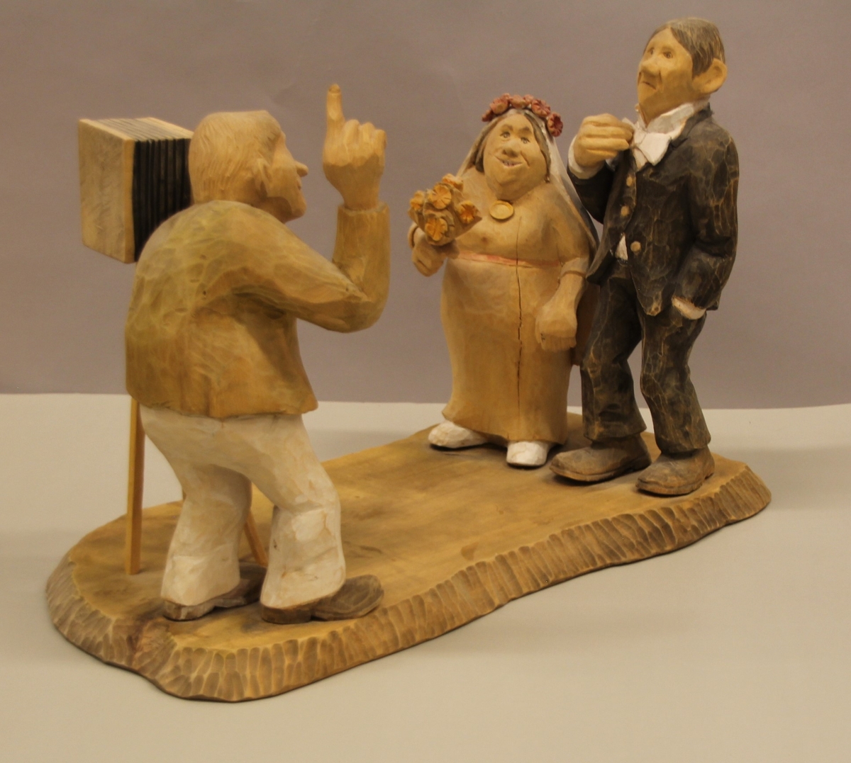 Skulptur som syner Arne Aas som tek bilete av eit brudepar. Skulpturen er skoren i tre.Tekst under:"Bjarne Walle fra Bamle laget denne gruppa på bestilling i fra fotografen Arne Aas i 1984" "Motiv: Arne Aas fotograferer brudepar". Bokstavane BW skore inn under skulpturen.