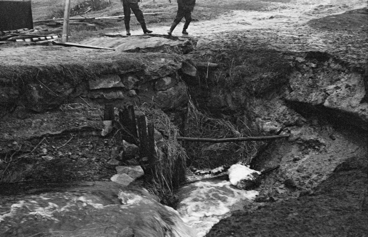 Dambrudd i Sagdammen i Sæteråa.  Fotografiet viser strømmende vann gjennom noe som later til å være en damarm av morenemasser.  Ved bildets øverkant skimtes beina til to menn. I 1958 ble det igangsatt et arbeid for å reparere og forsterke Sæterdammen slik at den skulle tåle biltrafikk. Kostnadene var kalkulert til 21 500 kroner. Sør-Odal kommune bidro med 10 000 kroner. Resten av kostnadene ble fordelt på Sæteråa tverrelvforening og skogeierne Sigvart Pran og Arnold Rørholt. 13 oppsittere skulle bidra med til sammen dagsverk.