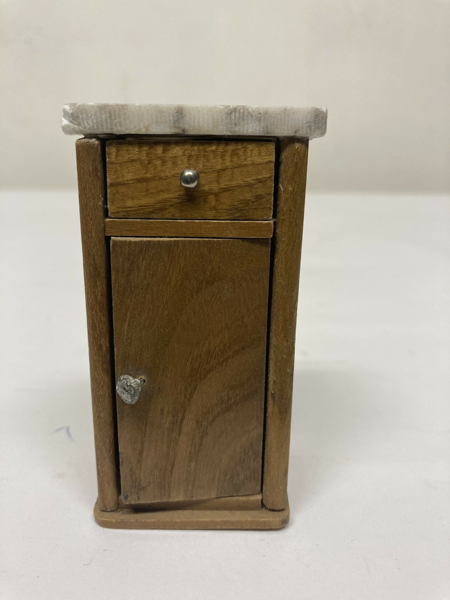 Vaskevannstol i toalettmøblement til dokkemøblement i treverk med steinplate. Plata er skadet. Dokkemøbler ble gitt til jenter til lek som forberedelse til voksenlivet.  