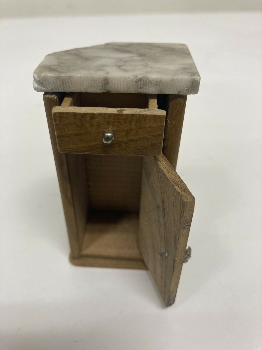 Vaskevannstol i toalettmøblement til dokkemøblement i treverk med steinplate. Plata er skadet. Dokkemøbler ble gitt til jenter til lek som forberedelse til voksenlivet.  