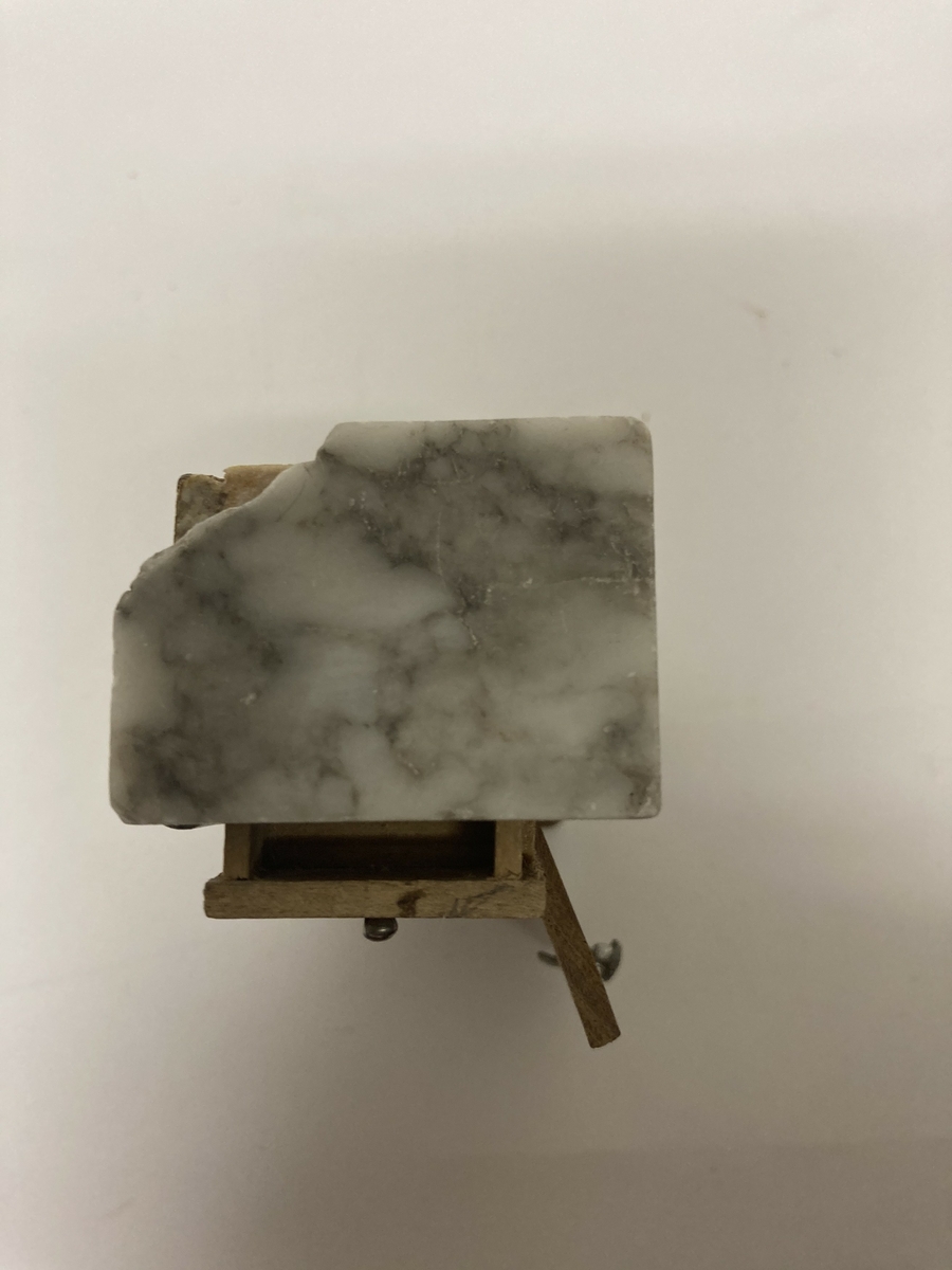 Vaskevannstol i toalettmøblement til dokkemøblement i treverk med steinplate. Plata er skadet. Dokkemøbler ble gitt til jenter til lek som forberedelse til voksenlivet.  