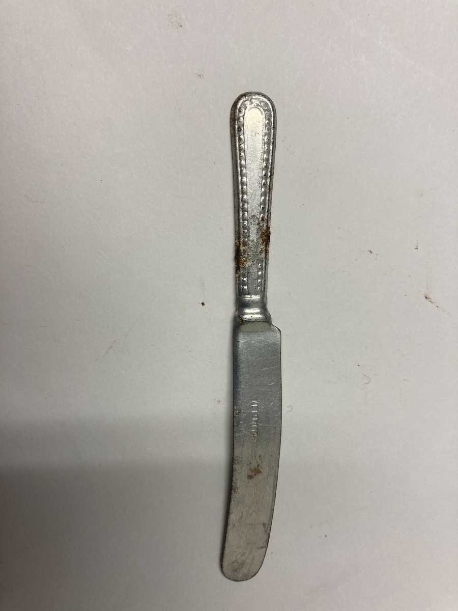 Kniv til bestikk i ni deler til dokkestell. Kniven har en skade. Dokkestell ble gitt til jenter til lek som forberedelse til voksenlivet. 