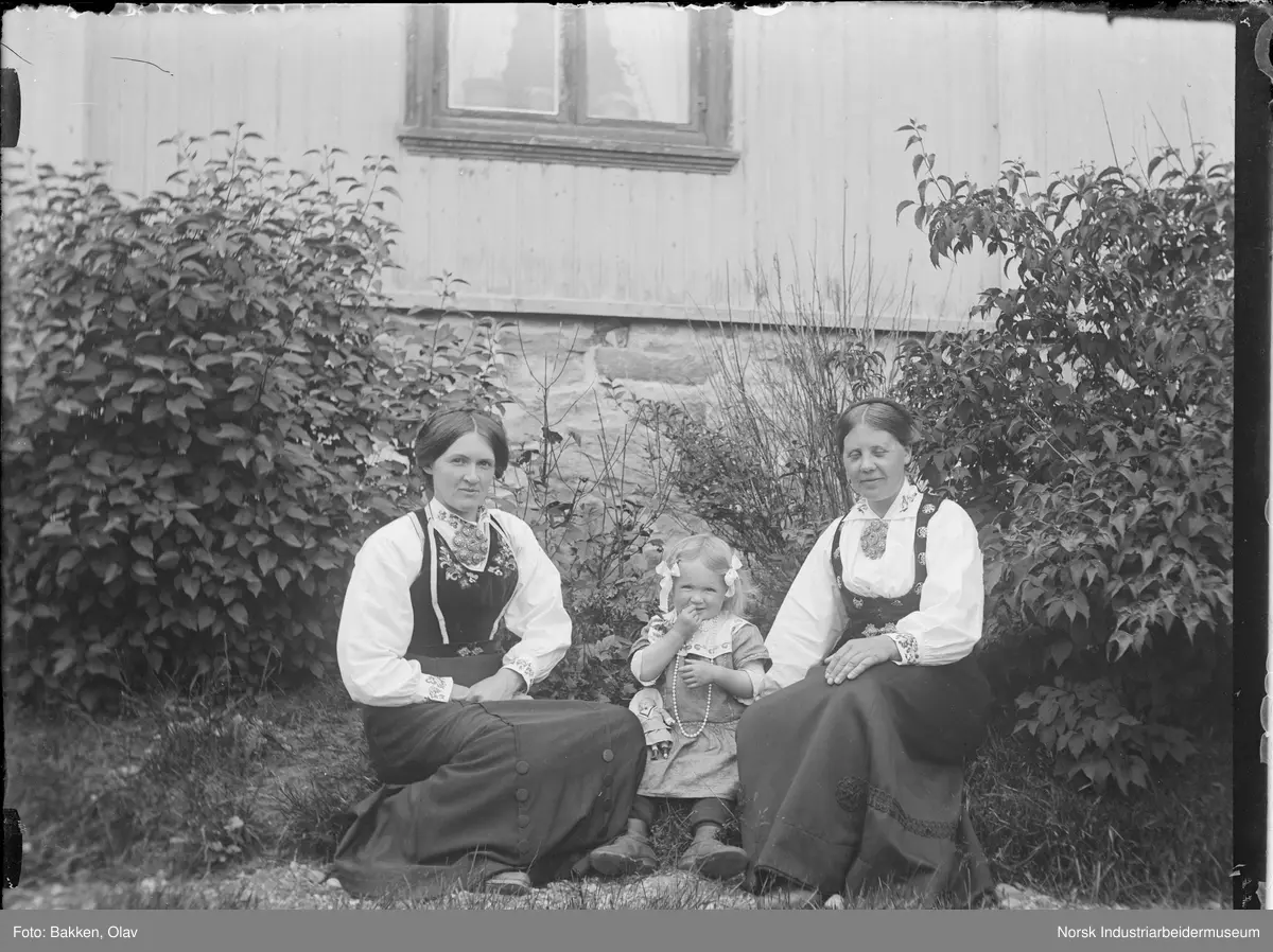 To kvinner og et jentebarn oppstilt i pentøy utenfor Klokkergården (lærerboligen).