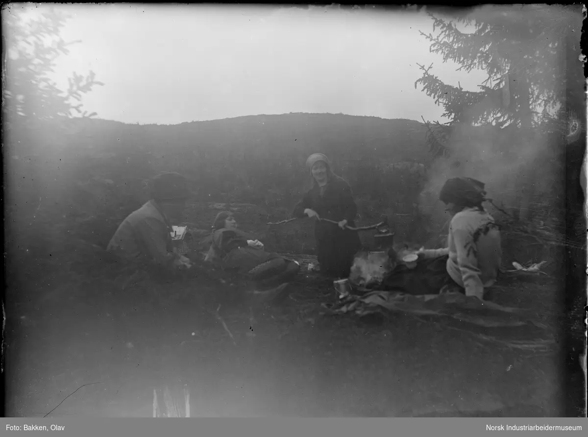 Fire kvinner koker kaffe på bål sittende i fjellområde.