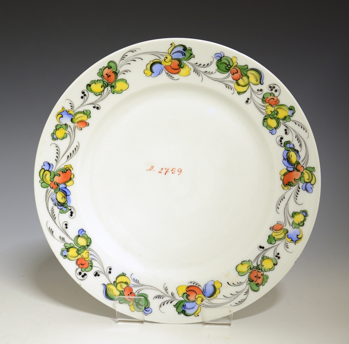 Prot: Flat tallerken av porselen, med glatt kant. Hvit glasur. Rosemalt fane i grønt, gult, blått, rødt og sort. Midt på speilen påskrift: "D. 2769"
Dekor: 2769