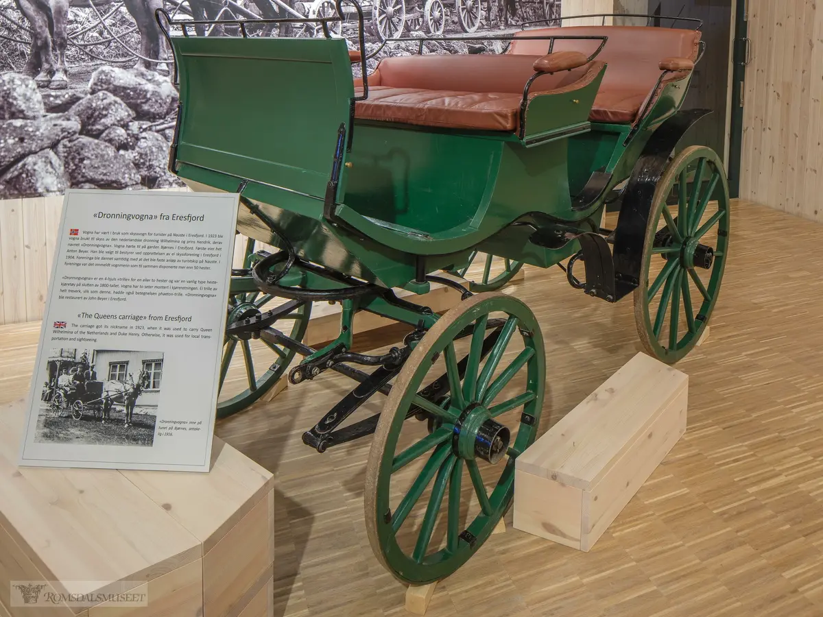 Fra utstillingen "i vognskjulet". .«Dronningvogna» fra Eresfjord.Vogna har vært i bruk som skyssvogn for turister på Nauste i Eresfjord. I 1923 ble vogna brukt under besøk av den nederlandske dronning Wilhelmina og prins Hendrik, derav navnet «Dronningvogna». Vogna hørte til på garden Bjørnes i Eresfjord...Den første eieren het Anton Beyer. Han ble valgt til bestyrer ved opprettelsen av ei skyssforening i Eresfjord i 1904. Foreninga ble dannet samtidig med at det ble faste anløp av turistskip på Nauste. I foreninga var det innmeldt vognmenn som til sammen disponerte mer enn 50 hester. ..«Dronningvogna» er en 4-hjuls «trille» for bruk med en eller to hester og var en vanlig type hestekjøretøy på slutten av 1800-tallet. Vogna har to seter montert i kjøreretningen. Ei trille av helt treverk, slik som denne, hadde også betegnelsen «phaeton-trille». «Dronningvogna» ble restaurert av John Beyer i Eresfjord.