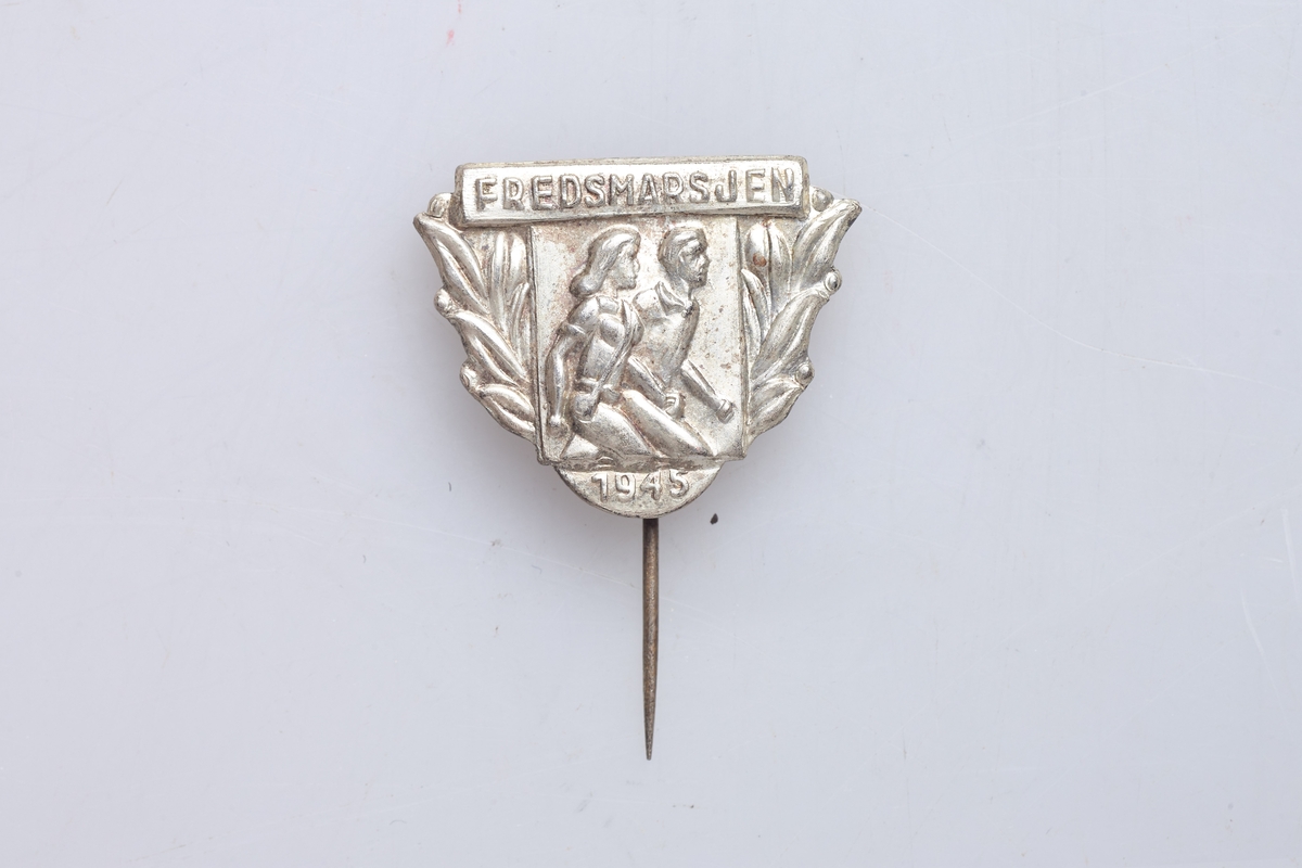 Nål for deltakelse i fredsmarsjen 1945. Nålen viser to personer som går. Støpt merke med påloddet nål.