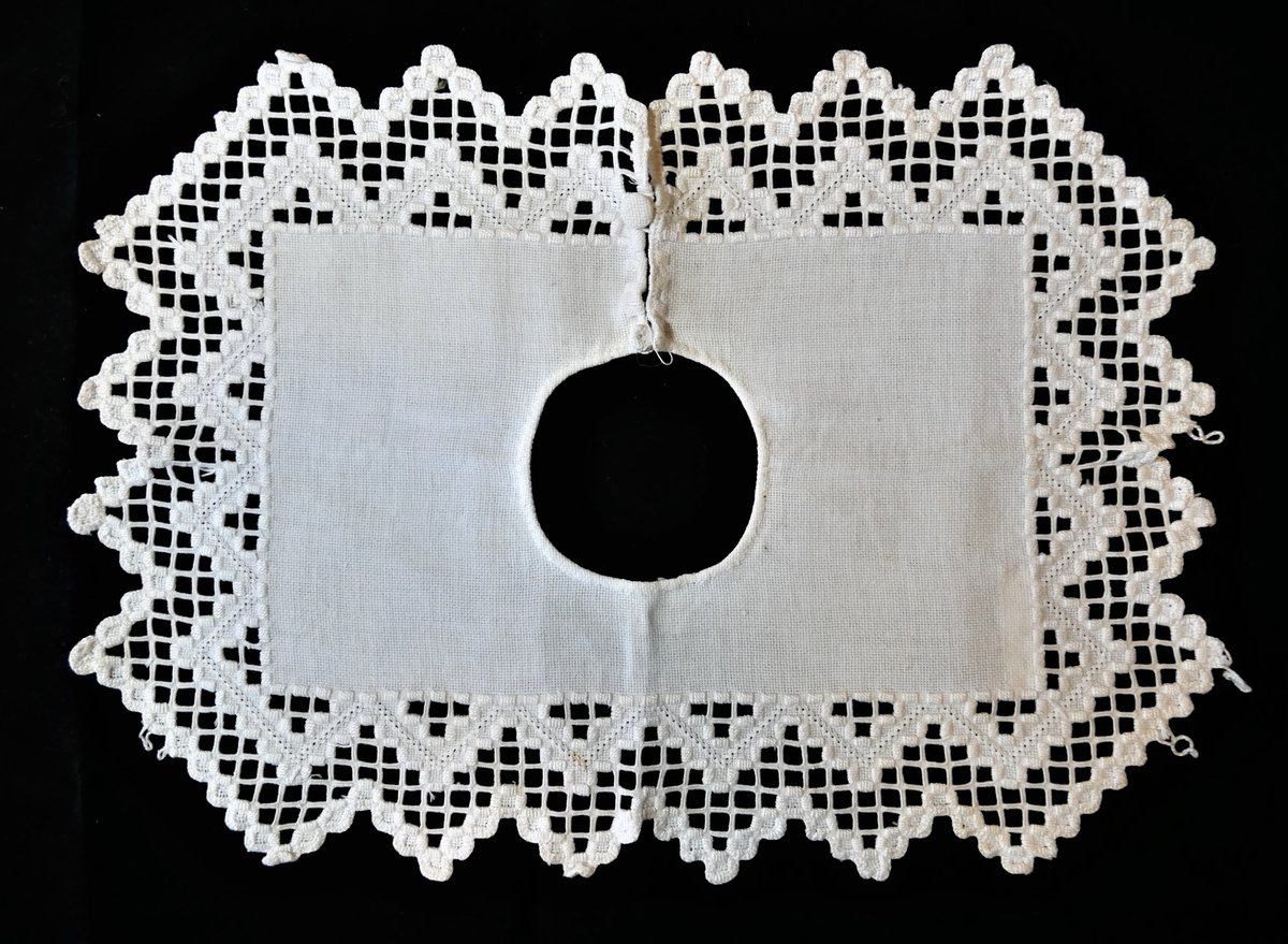 Ei smikke i bomull, laga av eitt stoffstykke. Dekorert med uttrekkssaum på yttekanten. Knepping i eine sida/skuldra.