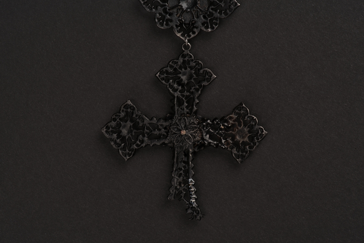 Svart halsband av gjutjärn.
Halsbandet består av omväxlande större och mindre utsirade länkar i nygotisk stil, som är sammanfästa med runda små länkar. Mitt fram hänger ett större likformat kors, som är något skadat. Spännet är utformat som två händer.