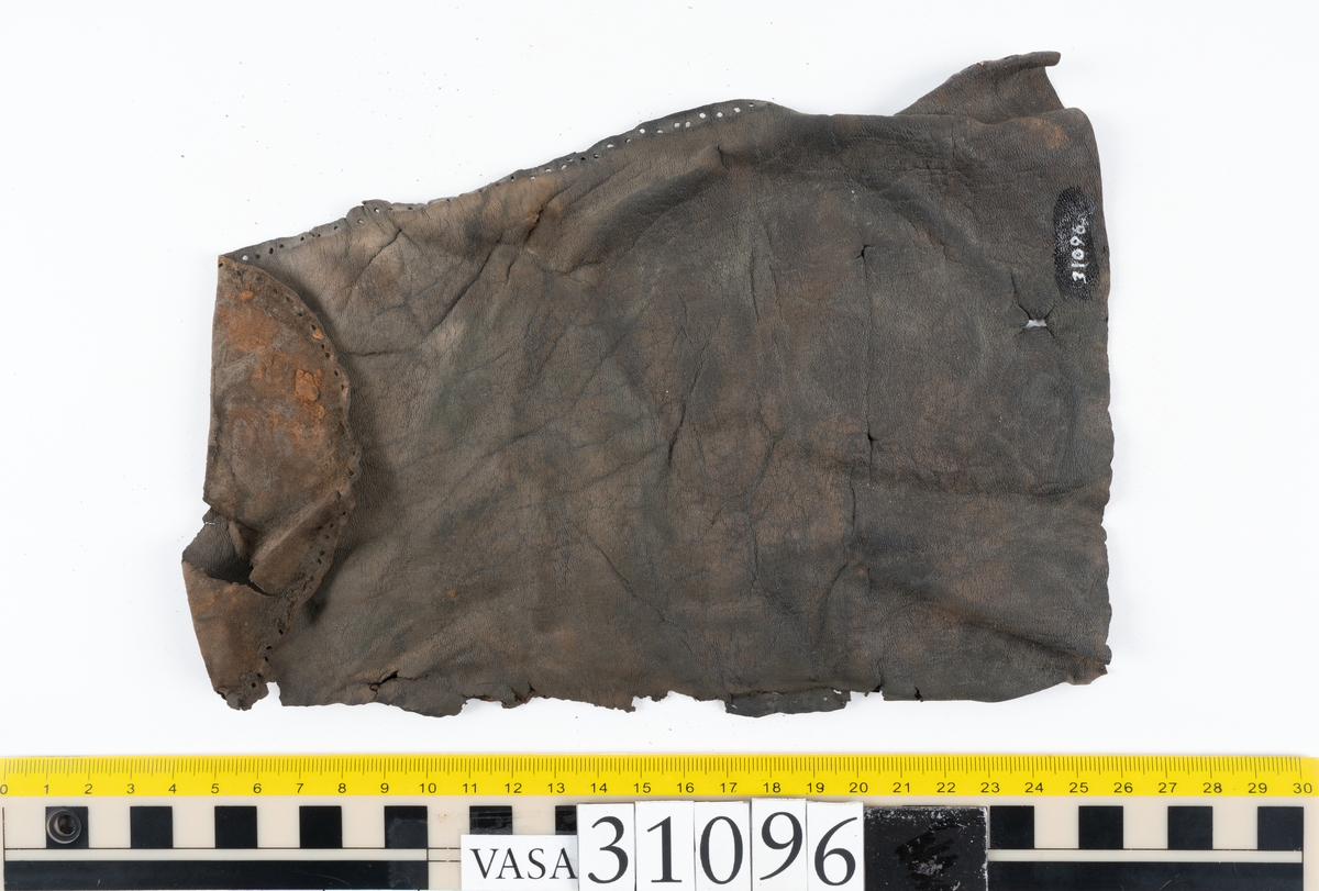 Fyra delar från en tumvante.
Vanten är skuren i två stycken, ett fram- och ett bakstycke, som varit sammanfogat med stygn.
Ett framstycke till en tumvante, fyndnummer 31096. Runt ytterkanterna löper stygnshål. Lädrets kött- och narvsida har släppt från varandra. Vanten har fläckvist rostliknande beläggningar. Lädret är tunt och sprött.
En vanttumme, fyndnummer 31096:1 Längs med ena sidan på vanttummen löper långsmala hål eller öppningar, två och två. Hålen kan härröra från en förstärkning som suttit fästad på vanttummen.
Triangelformat bakstycke till vanttumme, fyndnummer 31096:2. Lädret har skurits ut från vantens bakstycke. Stygnshål är synliga längs med två av sidorna.
Rektangulärt läderstycke, fyndnummer 31096:3. Längs med ytterkanterna löper srygnshål. Lädret är mjukt och narvytan tydlig. Lädret har börjat att spalta sig samt är försett med några rostliknande fläckar. Troligtvis har läderbiten fungerat som en förstärkning och suttit fästad på vantens in - eller utsida.