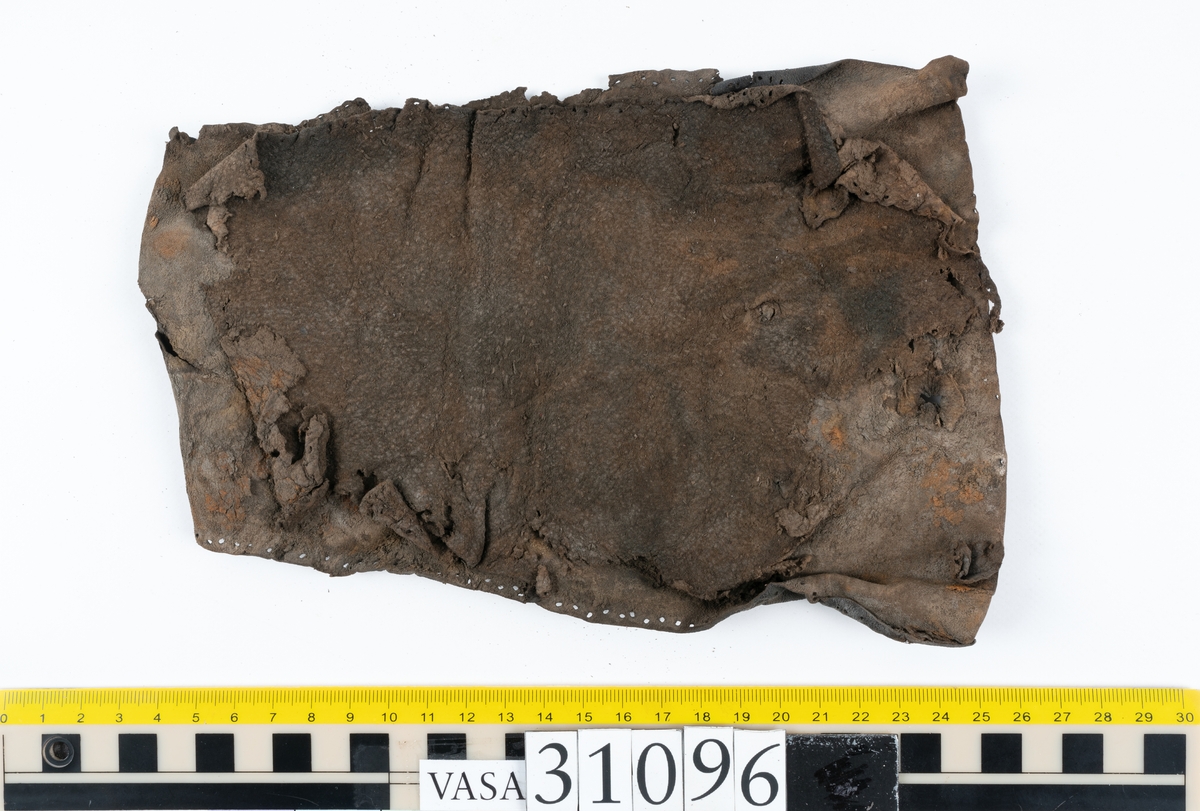 Fyra delar från en tumvante.
Vanten är skuren i två stycken, ett fram- och ett bakstycke, som varit sammanfogat med stygn.
Ett framstycke till en tumvante, fyndnummer 31096. Runt ytterkanterna löper stygnshål. Lädrets kött- och narvsida har släppt från varandra. Vanten har fläckvist rostliknande beläggningar. Lädret är tunt och sprött.
En vanttumme, fyndnummer 31096:1 Längs med ena sidan på vanttummen löper långsmala hål eller öppningar, två och två. Hålen kan härröra från en förstärkning som suttit fästad på vanttummen.
Triangelformat bakstycke till vanttumme, fyndnummer 31096:2. Lädret har skurits ut från vantens bakstycke. Stygnshål är synliga längs med två av sidorna.
Rektangulärt läderstycke, fyndnummer 31096:3. Längs med ytterkanterna löper srygnshål. Lädret är mjukt och narvytan tydlig. Lädret har börjat att spalta sig samt är försett med några rostliknande fläckar. Troligtvis har läderbiten fungerat som en förstärkning och suttit fästad på vantens in - eller utsida.