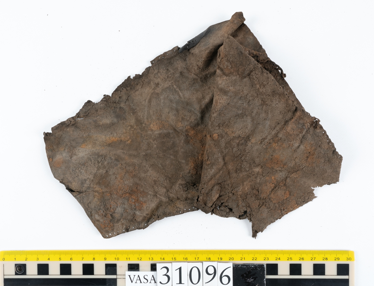 Fyra delar från en tumvante.
Vanten är skuren i två stycken, ett fram- och ett bakstycke, som varit sammanfogat med stygn.
Ett framstycke till en tumvante, fyndnummer 31096. Runt ytterkanterna löper stygnshål. Lädrets kött- och narvsida har släppt från varandra. Vanten har fläckvist rostliknande beläggningar. Lädret är tunt och sprött.
En vanttumme, fyndnummer 31096:1 Längs med ena sidan på vanttummen löper långsmala hål eller öppningar, två och två. Hålen kan härröra från en förstärkning som suttit fästad på vanttummen.
Triangelformat bakstycke till vanttumme, fyndnummer 31096:2. Lädret har skurits ut från vantens bakstycke. Stygnshål är synliga längs med två av sidorna.
Rektangulärt läderstycke, fyndnummer 31096:3. Längs med ytterkanterna löper srygnshål. Lädret är mjukt och narvytan tydlig. Lädret har börjat att spalta sig samt är försett med några rostliknande fläckar. Troligtvis har läderbiten fungerat som en förstärkning och suttit fästad på vantens in - eller utsida.