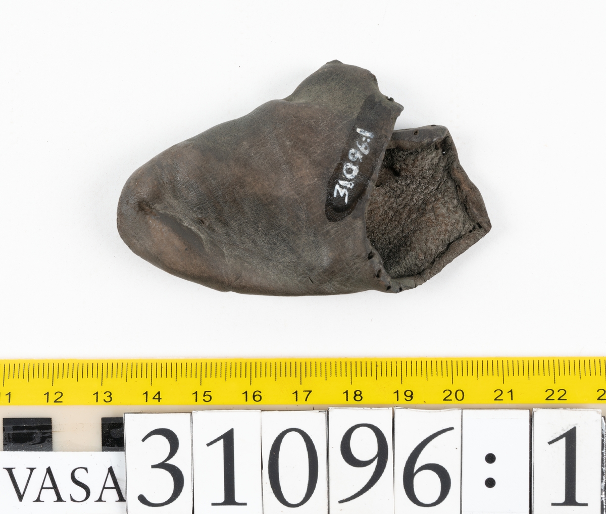 Fyra delar från en tumvante.
Vanten är skuren i två stycken, ett fram- och ett bakstycke, som varit sammanfogat med stygn.
Ett framstycke till en tumvante, fyndnummer 31096. Runt ytterkanterna löper stygnshål. Lädrets kött- och narvsida har släppt från varandra. Vanten har fläckvist rostliknande beläggningar. Lädret är tunt och sprött.
En vanttumme, fyndnummer 31096:1 Längs med ena sidan på vanttummen löper långsmala hål eller öppningar, två och två. Hålen kan härröra från en förstärkning som suttit fästad på vanttummen.
Triangelformat bakstycke till vanttumme, fyndnummer 31096:2. Lädret har skurits ut från vantens bakstycke. Stygnshål är synliga längs med två av sidorna.
Rektangulärt läderstycke, fyndnummer 31096:3. Längs med ytterkanterna löper srygnshål. Lädret är mjukt och narvytan tydlig. Lädret har börjat att spalta sig samt är försett med några rostliknande fläckar. Troligtvis har läderbiten fungerat som en förstärkning och suttit fästad på vantens in - eller utsida.