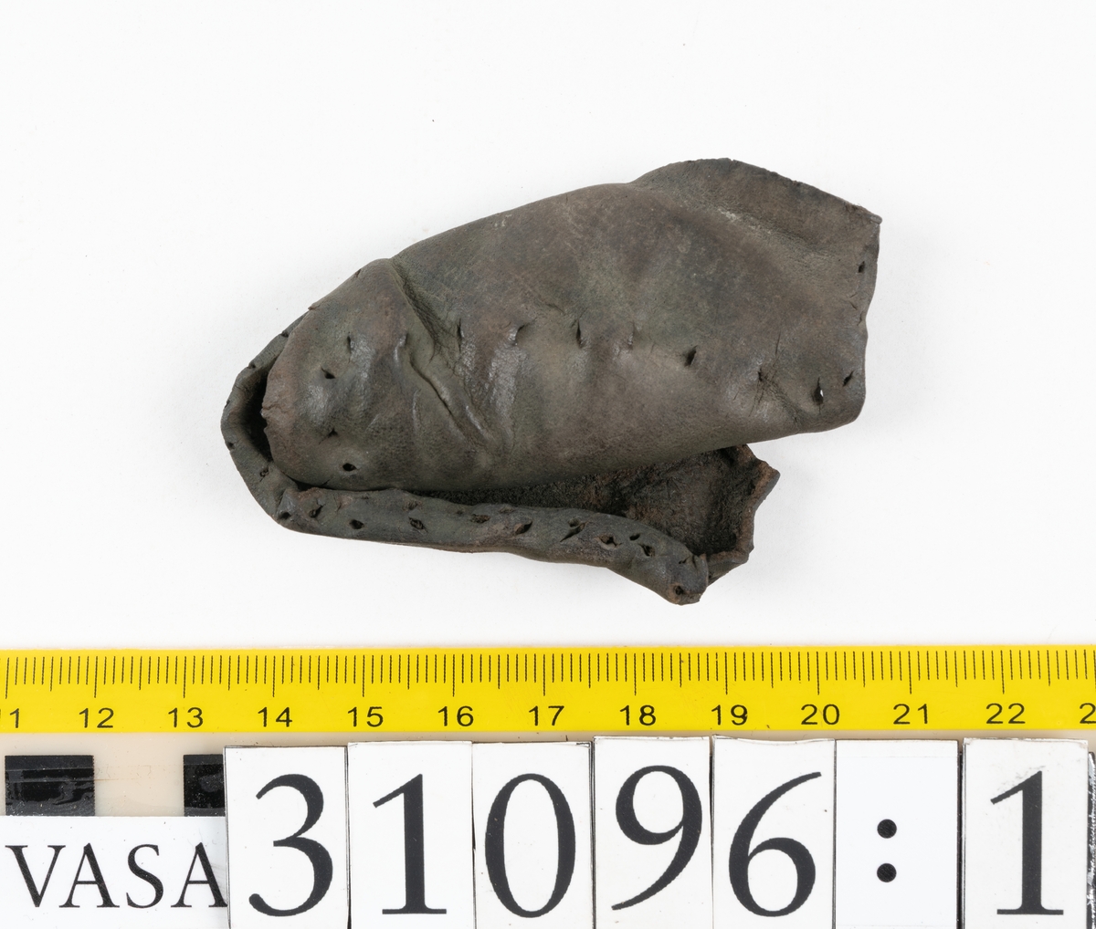 Fyra delar från en tumvante.
Vanten är skuren i två stycken, ett fram- och ett bakstycke, som varit sammanfogat med stygn.
Ett framstycke till en tumvante, fyndnummer 31096. Runt ytterkanterna löper stygnshål. Lädrets kött- och narvsida har släppt från varandra. Vanten har fläckvist rostliknande beläggningar. Lädret är tunt och sprött.
En vanttumme, fyndnummer 31096:1 Längs med ena sidan på vanttummen löper långsmala hål eller öppningar, två och två. Hålen kan härröra från en förstärkning som suttit fästad på vanttummen.
Triangelformat bakstycke till vanttumme, fyndnummer 31096:2. Lädret har skurits ut från vantens bakstycke. Stygnshål är synliga längs med två av sidorna.
Rektangulärt läderstycke, fyndnummer 31096:3. Längs med ytterkanterna löper srygnshål. Lädret är mjukt och narvytan tydlig. Lädret har börjat att spalta sig samt är försett med några rostliknande fläckar. Troligtvis har läderbiten fungerat som en förstärkning och suttit fästad på vantens in - eller utsida.