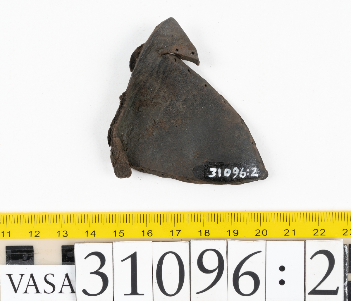 Fyra delar från en tumvante.
Vanten är skuren i två stycken, ett fram- och ett bakstycke, som varit sammanfogat med stygn.
Ett framstycke till en tumvante, fyndnummer 31096. Runt ytterkanterna löper stygnshål. Lädrets kött- och narvsida har släppt från varandra. Vanten har fläckvist rostliknande beläggningar. Lädret är tunt och sprött.
En vanttumme, fyndnummer 31096:1 Längs med ena sidan på vanttummen löper långsmala hål eller öppningar, två och två. Hålen kan härröra från en förstärkning som suttit fästad på vanttummen.
Triangelformat bakstycke till vanttumme, fyndnummer 31096:2. Lädret har skurits ut från vantens bakstycke. Stygnshål är synliga längs med två av sidorna.
Rektangulärt läderstycke, fyndnummer 31096:3. Längs med ytterkanterna löper srygnshål. Lädret är mjukt och narvytan tydlig. Lädret har börjat att spalta sig samt är försett med några rostliknande fläckar. Troligtvis har läderbiten fungerat som en förstärkning och suttit fästad på vantens in - eller utsida.