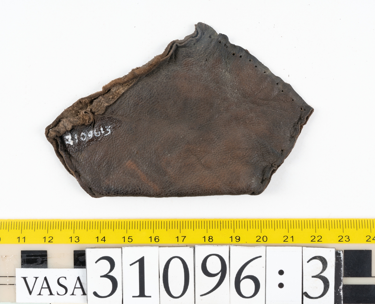 Fyra delar från en tumvante.
Vanten är skuren i två stycken, ett fram- och ett bakstycke, som varit sammanfogat med stygn.
Ett framstycke till en tumvante, fyndnummer 31096. Runt ytterkanterna löper stygnshål. Lädrets kött- och narvsida har släppt från varandra. Vanten har fläckvist rostliknande beläggningar. Lädret är tunt och sprött.
En vanttumme, fyndnummer 31096:1 Längs med ena sidan på vanttummen löper långsmala hål eller öppningar, två och två. Hålen kan härröra från en förstärkning som suttit fästad på vanttummen.
Triangelformat bakstycke till vanttumme, fyndnummer 31096:2. Lädret har skurits ut från vantens bakstycke. Stygnshål är synliga längs med två av sidorna.
Rektangulärt läderstycke, fyndnummer 31096:3. Längs med ytterkanterna löper srygnshål. Lädret är mjukt och narvytan tydlig. Lädret har börjat att spalta sig samt är försett med några rostliknande fläckar. Troligtvis har läderbiten fungerat som en förstärkning och suttit fästad på vantens in - eller utsida.