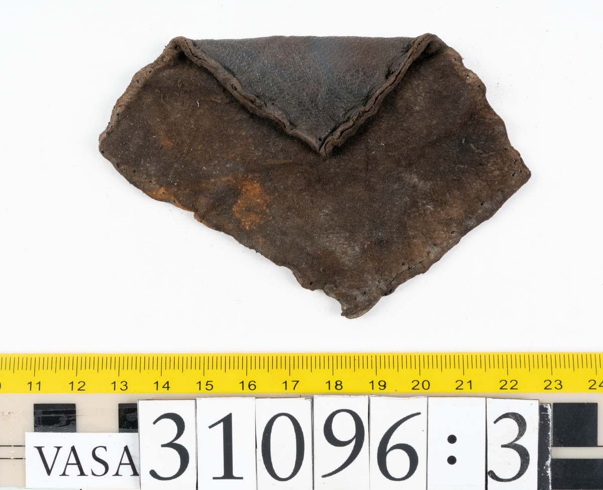 Fyra delar från en tumvante.
Vanten är skuren i två stycken, ett fram- och ett bakstycke, som varit sammanfogat med stygn.
Ett framstycke till en tumvante, fyndnummer 31096. Runt ytterkanterna löper stygnshål. Lädrets kött- och narvsida har släppt från varandra. Vanten har fläckvist rostliknande beläggningar. Lädret är tunt och sprött.
En vanttumme, fyndnummer 31096:1 Längs med ena sidan på vanttummen löper långsmala hål eller öppningar, två och två. Hålen kan härröra från en förstärkning som suttit fästad på vanttummen.
Triangelformat bakstycke till vanttumme, fyndnummer 31096:2. Lädret har skurits ut från vantens bakstycke. Stygnshål är synliga längs med två av sidorna.
Rektangulärt läderstycke, fyndnummer 31096:3. Längs med ytterkanterna löper srygnshål. Lädret är mjukt och narvytan tydlig. Lädret har börjat att spalta sig samt är försett med några rostliknande fläckar. Troligtvis har läderbiten fungerat som en förstärkning och suttit fästad på vantens in - eller utsida.