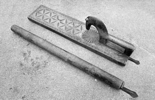 Utskåret mangletre med hestehåndtak og rullepinne liggende ved siden av.