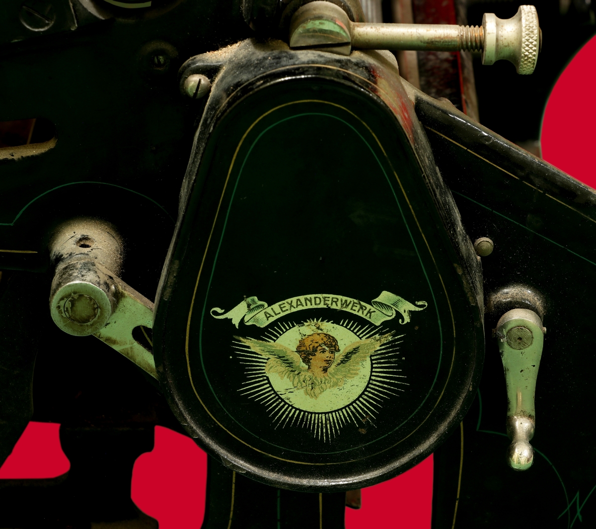 Kopieringsmaskin i svartmålad metall med dekorlinjer målade i guld och grönt. På vänster sida en logga där det står Alexanderwerk och under det en ängel. På vänster sida också en spak i vitmetall. På ovansidan en platt skiva, under den en räfflad rulle. På höger sida en ett vrede med handtag i svartmålat trä.