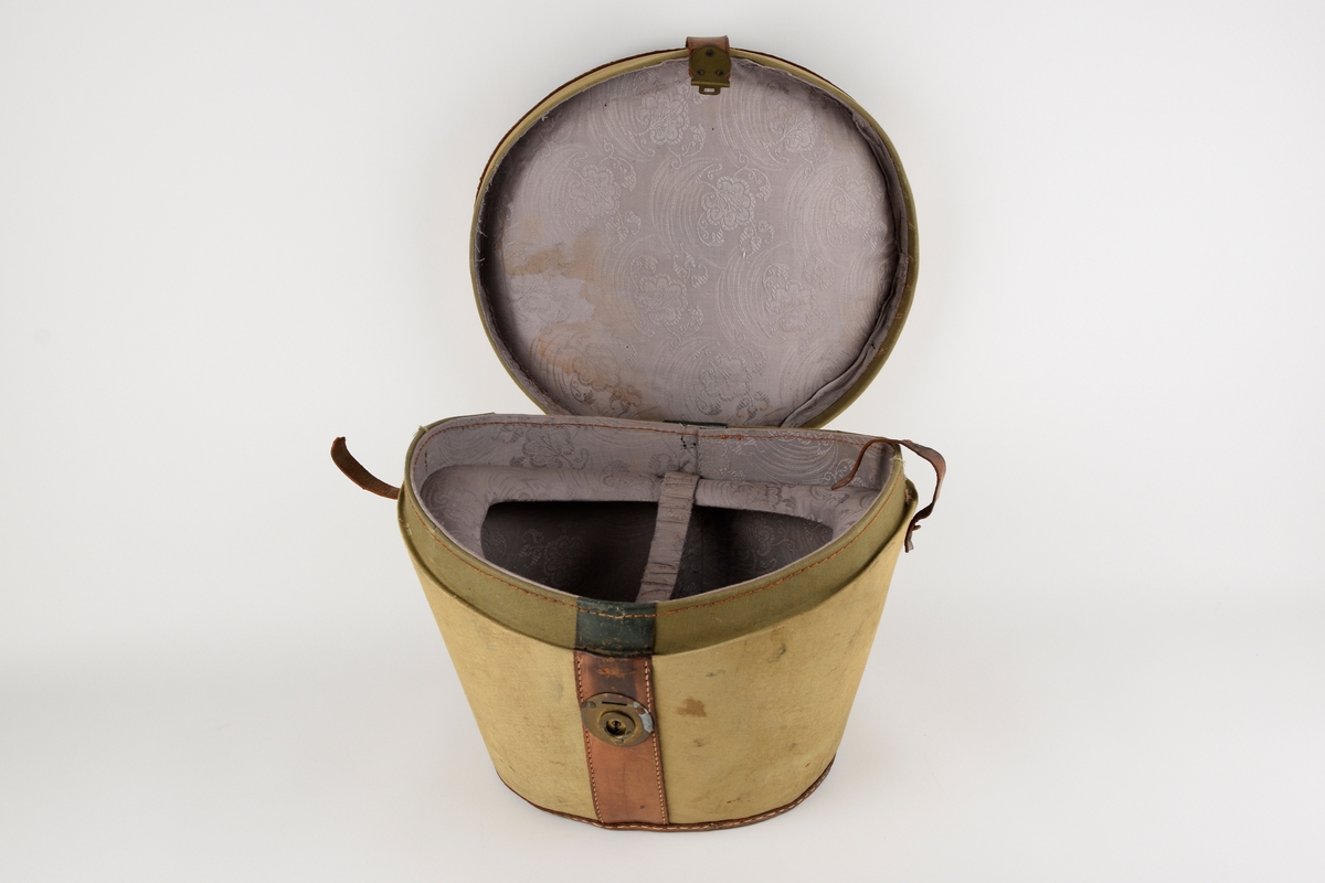 Hatteeske til flosshatt. 

Oval grunnflate. Sidene på esken skrår utover. Buet lokk. Reimer og kanter av skinn. Lokket er hengslet med skinnreim. Reimen går over lokket og ender i lås i front. Bærehåndtak av skinn på lokket, der endene har metallhemper for festing av reimer fra eskekroppen. Innvendig kledd med grå, mønstret tekstil. To reimer med trykknapp går på tvers av esken innvendig.