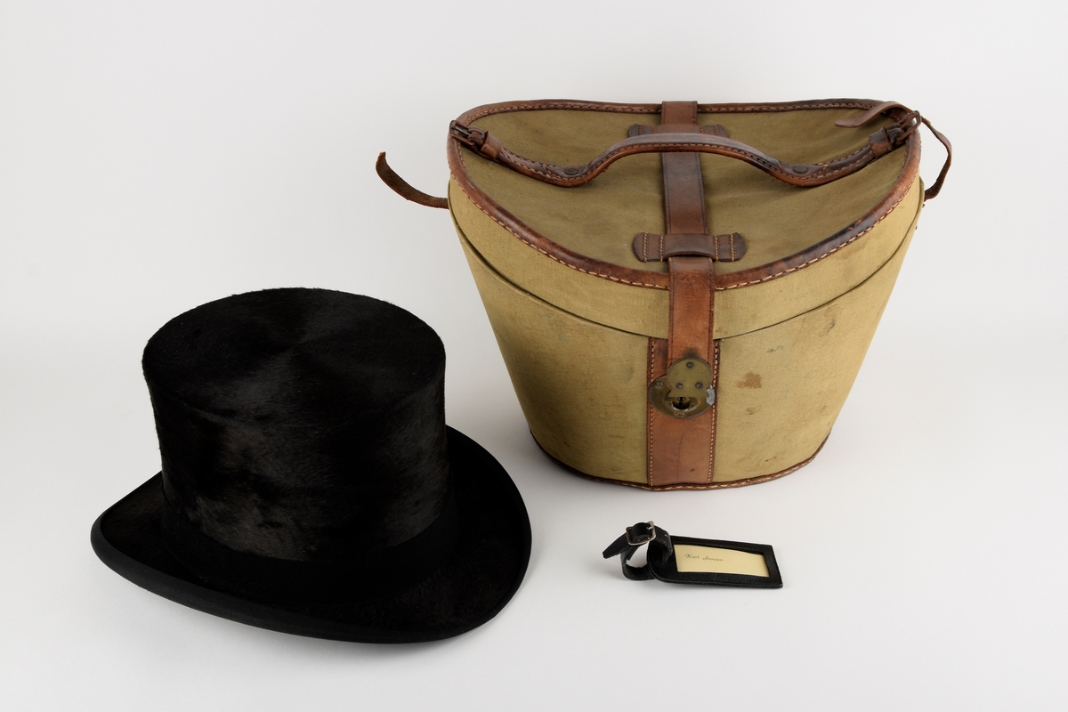 Hatteeske til flosshatt. 

Oval grunnflate. Sidene på esken skrår utover. Buet lokk. Reimer og kanter av skinn. Lokket er hengslet med skinnreim. Reimen går over lokket og ender i lås i front. Bærehåndtak av skinn på lokket, der endene har metallhemper for festing av reimer fra eskekroppen. Innvendig kledd med grå, mønstret tekstil. To reimer med trykknapp går på tvers av esken innvendig.