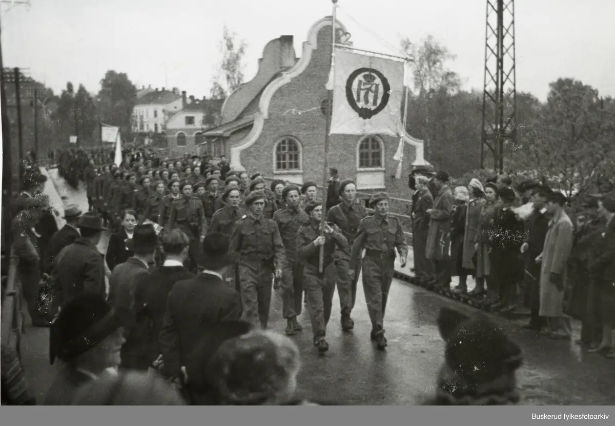Hjemmestyrkene defilerer i Hønefoss 17. mai 1945. Ola Kvernstue med fanen, Georg Rua i spiss Karl Larsson, Kåre Hellum, Reidar Solbakken