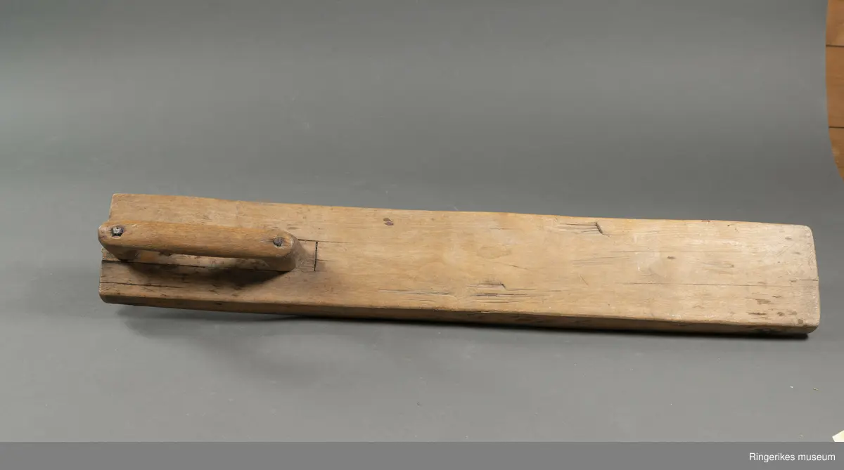 Mangletre av ubehandlet treverk. Håndtaket er festet med nagler. Mangletreet er ikke dekorert, og håndtaket har ikke spesiell utforming.