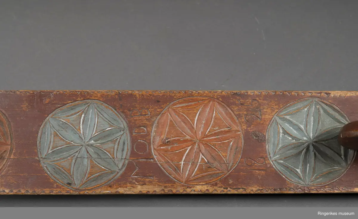 Hoveddelen av mangletreet er laget av massivt tre, med en sprekk i nederste del. Håndtaket er formet som en stilisert hest, uten detaljer som man og ører. Håndtaket er nedfelt i selve mangletreet. Oppheng med øyeskrue er laget senere. Mangletreet er dekorert med 4 store rosetter. Diameter på rosetter er på 9.3 cm. De har 6 kronblad. Rosettene er laget med karveskurd. Enkel karveskurd langs kanten.