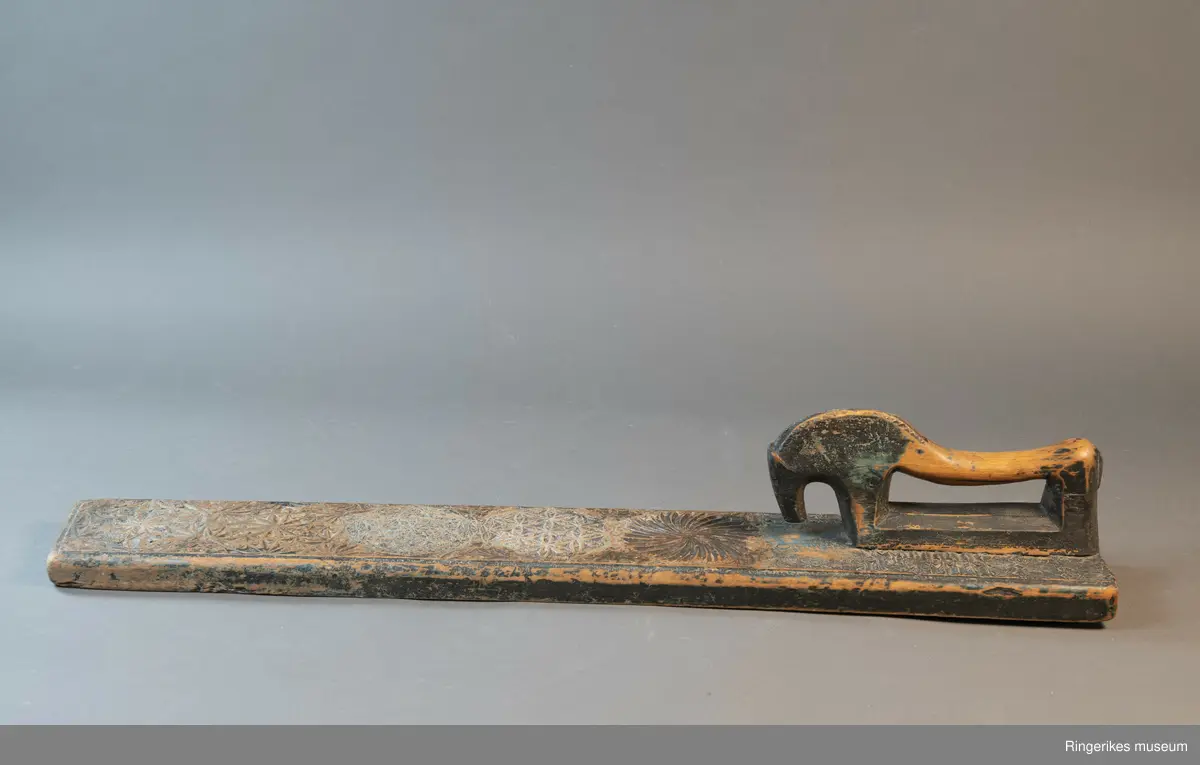 Mangletre med innfelt håndtak formet som en hest. Mangletreet er dekorert med treskurd. Hovedmønsteret består av 5 sirkler hvorav 1 har sagbladtagger inni,  2 med seksbladroser inni og 2 med flere seksbladroser inni sirklene. Rundt håndtaket er det dekorert med trekanter og diamantformer. Under hodet på hesten er det risset inn ANO 1776. Mangletreet fremstår som veldig slitt og godt brukt. Det har opprinnelig vært malt og rester av fargene blå, rød og grønn er synlige.