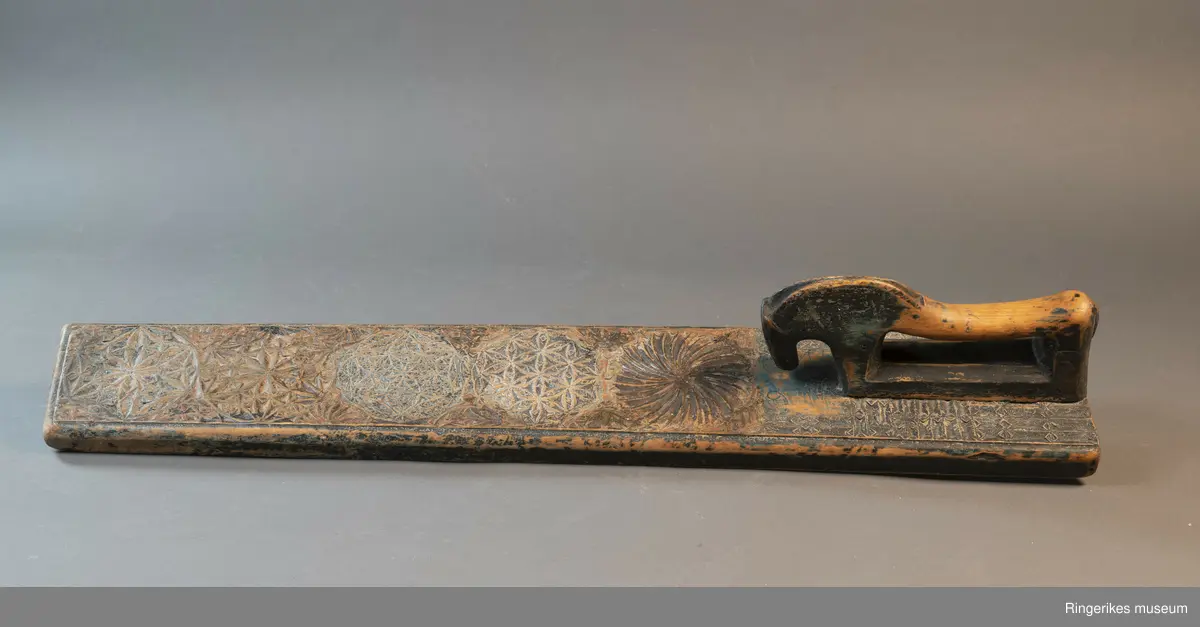 Mangletre med innfelt håndtak formet som en hest. Mangletreet er dekorert med treskurd. Hovedmønsteret består av 5 sirkler hvorav 1 har sagbladtagger inni,  2 med seksbladroser inni og 2 med flere seksbladroser inni sirklene. Rundt håndtaket er det dekorert med trekanter og diamantformer. Under hodet på hesten er det risset inn ANO 1776. Mangletreet fremstår som veldig slitt og godt brukt. Det har opprinnelig vært malt og rester av fargene blå, rød og grønn er synlige.