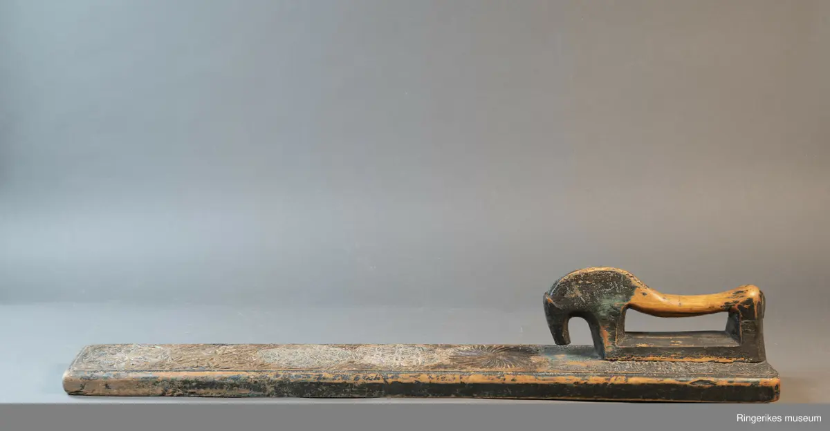 Mangletre med innfelt håndtak formet som en hest. Mangletreet er dekorert med treskurd. Hovedmønsteret består av 5 sirkler hvorav 1 har sagbladtagger inni,  2 med seksbladroser inni og 2 med flere seksbladroser inni sirklene. Rundt håndtaket er det dekorert med trekanter og diamantformer. Under hodet på hesten er det risset inn ANO 1776. Mangletreet fremstår som veldig slitt og godt brukt. Det har opprinnelig vært malt og rester av fargene blå, rød og grønn er synlige.