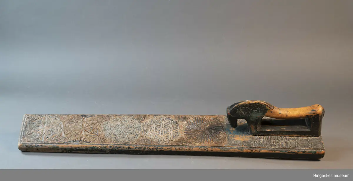 Mangletre med innfelt håndtak formet som en hest. Mangletreet er dekorert med treskurd. Hovedmønsteret består av 5 sirkler hvorav 1 har sagbladtagger inni,  2 med seksbladroser inni og 2 med flere seksbladroser inni sirklene. Rundt håndtaket er det dekorert med trekanter og diamantformer. Under hodet på hesten er det risset inn ANO 1776. Mangletreet fremstår som veldig slitt og godt brukt. Det har opprinnelig vært malt og rester av fargene blå, rød og grønn er synlige.