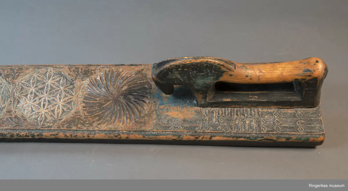 Mangletre med innfelt håndtak formet som en hest. Mangletreet er dekorert med treskurd. Hovedmønsteret består av 5 sirkler hvorav 1 har sagbladtagger inni,  2 med seksbladroser inni og 2 med flere seksbladroser inni sirklene. Rundt håndtaket er det dekorert med trekanter og diamantformer. Under hodet på hesten er det risset inn ANO 1776. Mangletreet fremstår som veldig slitt og godt brukt. Det har opprinnelig vært malt og rester av fargene blå, rød og grønn er synlige.