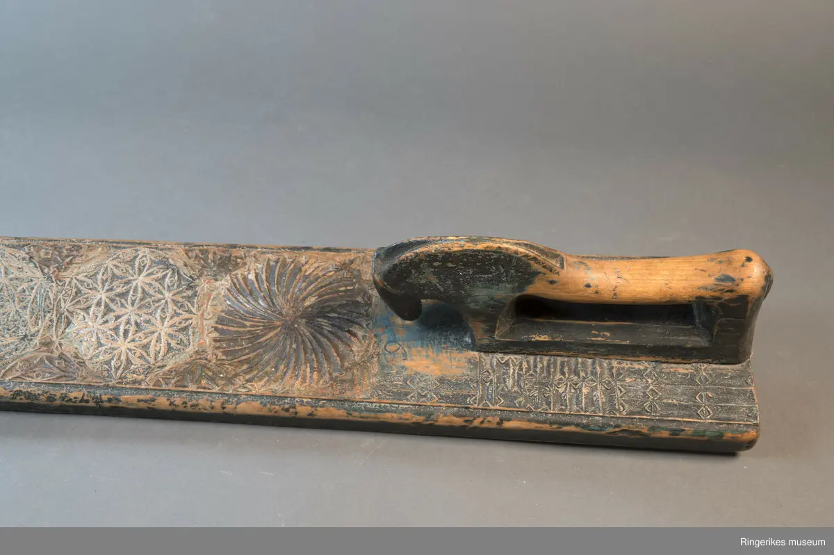 Mangletre med innfelt håndtak formet som en hest. Mangletreet er dekorert med treskurd. Hovedmønsteret består av 5 sirkler hvorav 1 har sagbladtagger inni,  2 med seksbladroser inni og 2 med flere seksbladroser inni sirklene. Rundt håndtaket er det dekorert med trekanter og diamantformer. Under hodet på hesten er det risset inn ANO 1776. Mangletreet fremstår som veldig slitt og godt brukt. Det har opprinnelig vært malt og rester av fargene blå, rød og grønn er synlige.