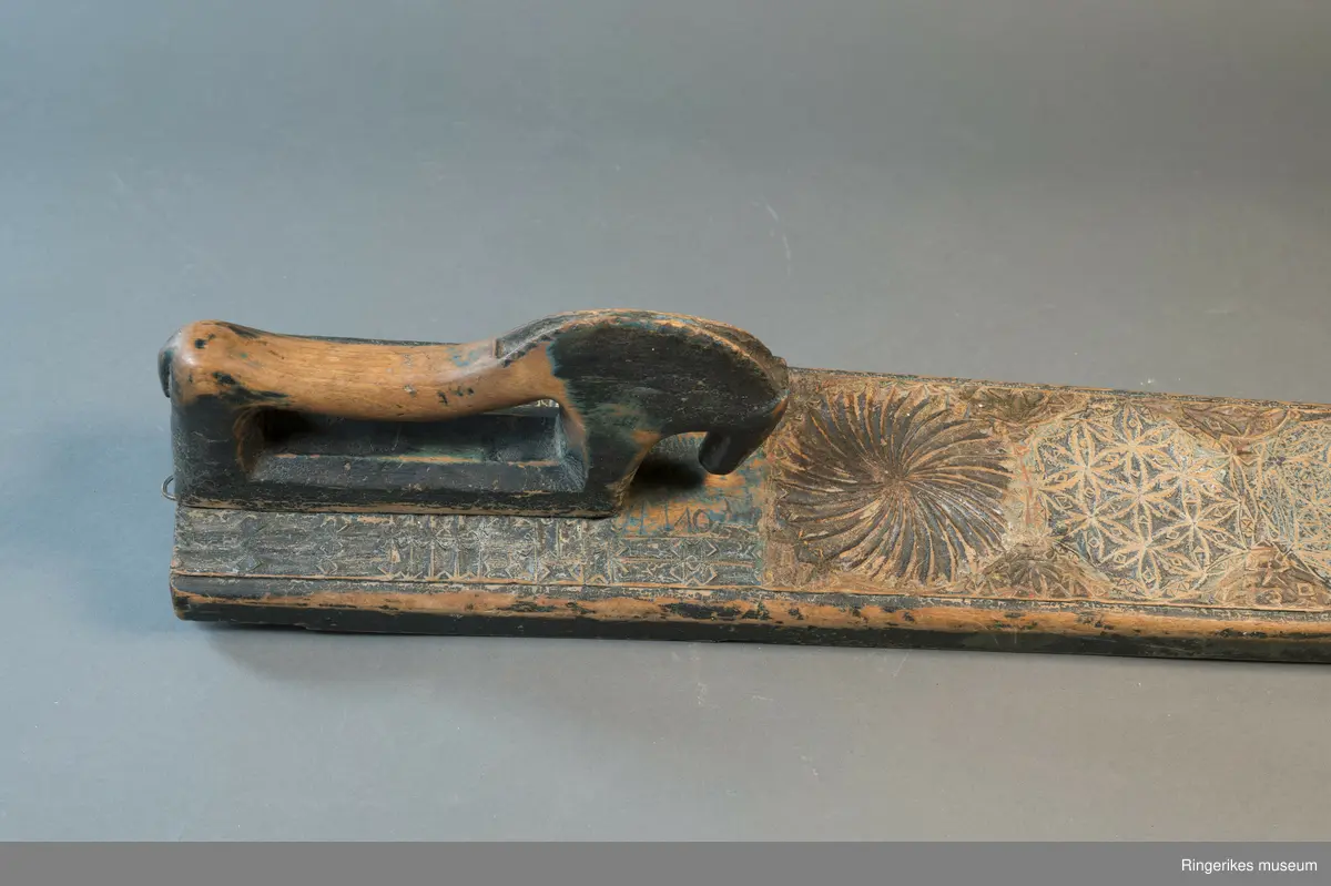 Mangletre med innfelt håndtak formet som en hest. Mangletreet er dekorert med treskurd. Hovedmønsteret består av 5 sirkler hvorav 1 har sagbladtagger inni,  2 med seksbladroser inni og 2 med flere seksbladroser inni sirklene. Rundt håndtaket er det dekorert med trekanter og diamantformer. Under hodet på hesten er det risset inn ANO 1776. Mangletreet fremstår som veldig slitt og godt brukt. Det har opprinnelig vært malt og rester av fargene blå, rød og grønn er synlige.