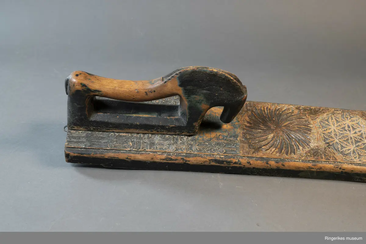 Mangletre med innfelt håndtak formet som en hest. Mangletreet er dekorert med treskurd. Hovedmønsteret består av 5 sirkler hvorav 1 har sagbladtagger inni,  2 med seksbladroser inni og 2 med flere seksbladroser inni sirklene. Rundt håndtaket er det dekorert med trekanter og diamantformer. Under hodet på hesten er det risset inn ANO 1776. Mangletreet fremstår som veldig slitt og godt brukt. Det har opprinnelig vært malt og rester av fargene blå, rød og grønn er synlige.