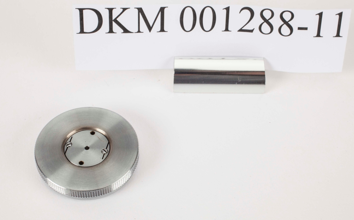 En rund metallskive. Den ligger i etuiet DKM 1288-13.
