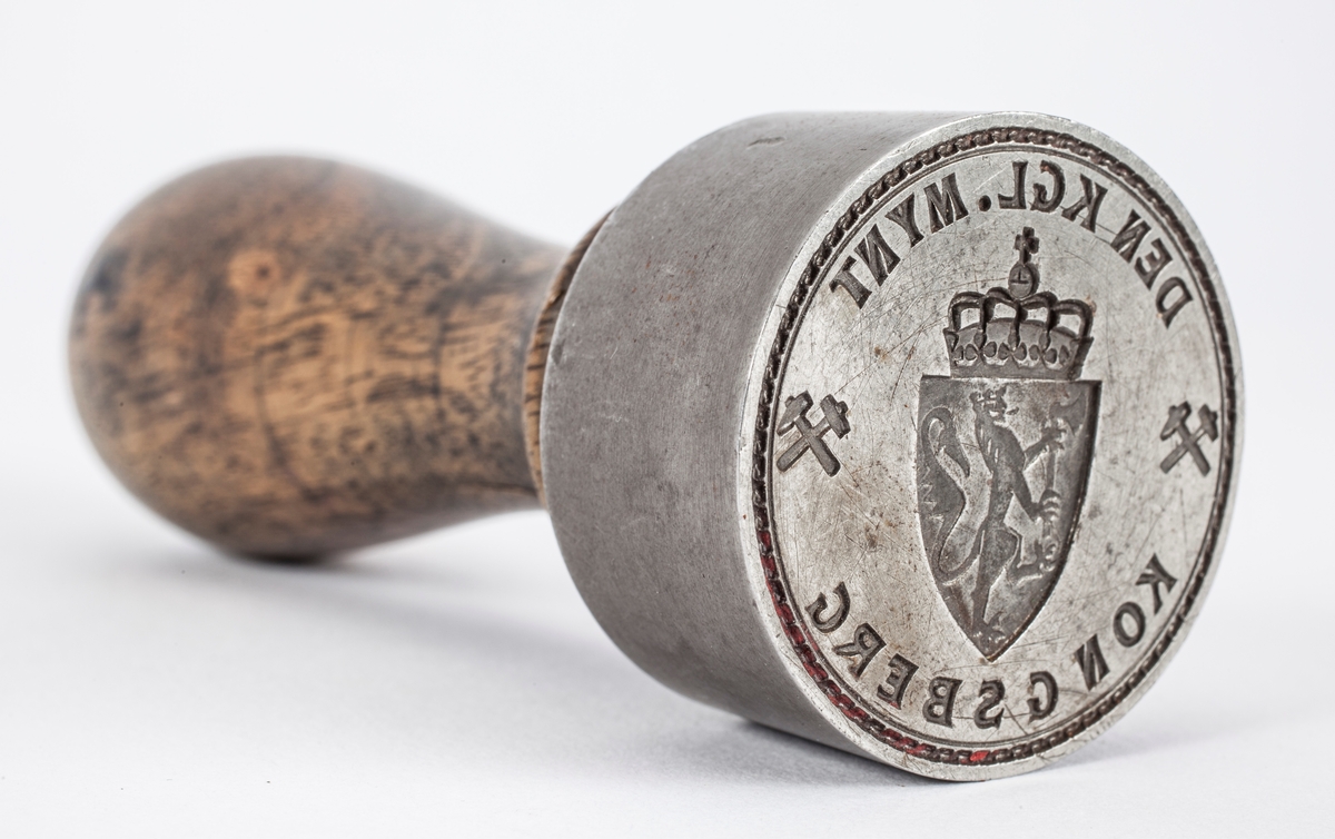 Norges riksvåpen, løve med øks og krone på ett skjold med krone over. På hver side er symbolet med hammer og feisel i kryss.