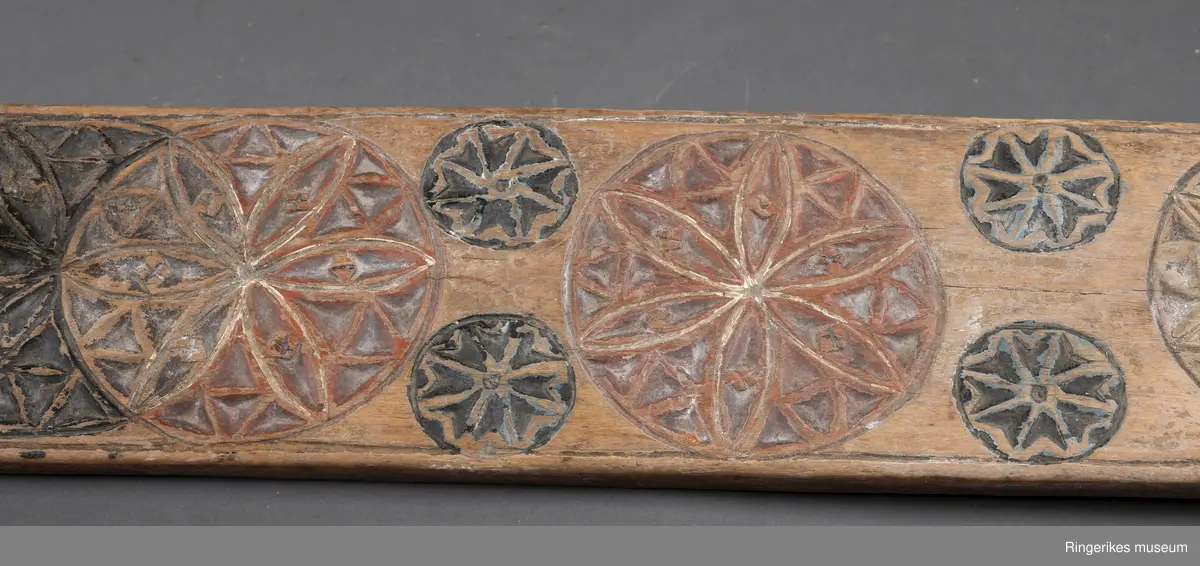 Mangletre med innfelt håndtak formet som en hest. Mangletreet er dekorert med treskurd hvor hovedmønsteret består av 4 sirkler med seksbladroser inni. 2 av sirklene står delvis inni hverandre. 4 små sirkler med åttebladroser er plassert mellom de store sirklene. Sirklene har opprinnelig vært malt og fremstår i dag som røde og svarte. På den ene siden ved håndtaket er det påmalt 1785 og på den andre siden GGD.