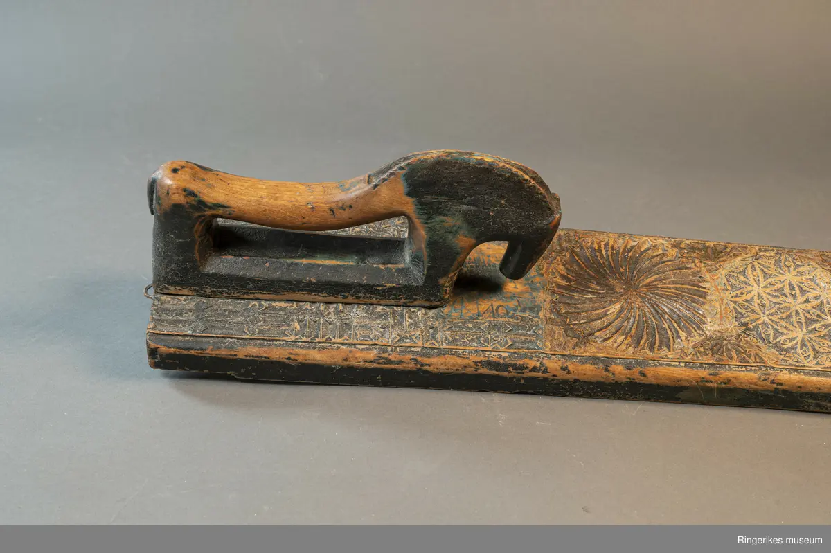 Mangletreet er dekorert med rosetter i mange forskjellige størrelser. Håndtaket er formet som en hest. Hesten har såvidt ører, øyne og munn. Hodet er stort og grovt. Øverst på mangletreet er det festet et oppheng av metall. Det er også rester av et annet oppheng, av strye eller hamp. Hesten er innfelt i mangletreet, resten av mangletreet er laget av massivt tre. Hesten har løsnet fra underlaget, ser ut som om den er festet med en treplugg. Mangletreet er dekorert med rosetter i karveskurd. Nederst er det en kvart rosett i hvert hjørne, med radius på 3 cm. Så kommer en stor rosett med diameter på 9.7 cm. Langs kanten er det to nye halve rosetter på hver side, og en i midten. Den i midten har diameter på 8 cm. De halve har diameter fra 5 cm til 7 cm. (Sett fra hesten: nederst til høyre: 5 cm, øverst til høyre: 6 cm, nederst til venstre: 6 cm, øverst til venstre: 7 cm. Under rosetten i midten står initialene OPD. Deretter kommer en stor rosett, diameter 12.5 cm. Så kommer to små, begge har diameter på 6 cm. Den største rosetten har diameter på 13.5 cm, og er nærmest hesten. Alle unntatt en rosett er dekorert med blomstermotiv. Den ene (halv rosett, øverst til høyre, 5 cm) er dekorert med buede streker. Ellers er det både i og rundt rosettene dekorert med små utskårne trekanter.