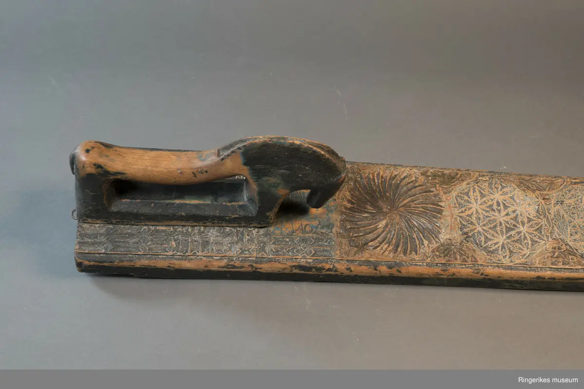 Mangletreet er dekorert med rosetter i mange forskjellige størrelser. Håndtaket er formet som en hest. Hesten har såvidt ører, øyne og munn. Hodet er stort og grovt. Øverst på mangletreet er det festet et oppheng av metall. Det er også rester av et annet oppheng, av strye eller hamp. Hesten er innfelt i mangletreet, resten av mangletreet er laget av massivt tre. Hesten har løsnet fra underlaget, ser ut som om den er festet med en treplugg. Mangletreet er dekorert med rosetter i karveskurd. Nederst er det en kvart rosett i hvert hjørne, med radius på 3 cm. Så kommer en stor rosett med diameter på 9.7 cm. Langs kanten er det to nye halve rosetter på hver side, og en i midten. Den i midten har diameter på 8 cm. De halve har diameter fra 5 cm til 7 cm. (Sett fra hesten: nederst til høyre: 5 cm, øverst til høyre: 6 cm, nederst til venstre: 6 cm, øverst til venstre: 7 cm. Under rosetten i midten står initialene OPD. Deretter kommer en stor rosett, diameter 12.5 cm. Så kommer to små, begge har diameter på 6 cm. Den største rosetten har diameter på 13.5 cm, og er nærmest hesten. Alle unntatt en rosett er dekorert med blomstermotiv. Den ene (halv rosett, øverst til høyre, 5 cm) er dekorert med buede streker. Ellers er det både i og rundt rosettene dekorert med små utskårne trekanter.