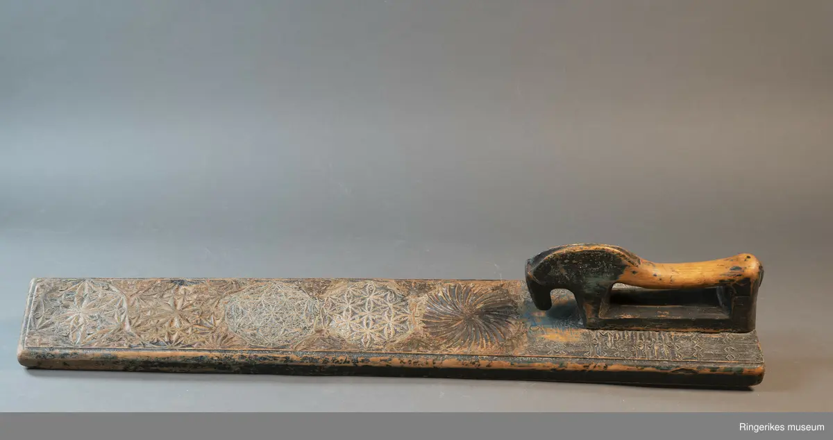 Mangletreet er dekorert med rosetter i mange forskjellige størrelser. Håndtaket er formet som en hest. Hesten har såvidt ører, øyne og munn. Hodet er stort og grovt. Øverst på mangletreet er det festet et oppheng av metall. Det er også rester av et annet oppheng, av strye eller hamp. Hesten er innfelt i mangletreet, resten av mangletreet er laget av massivt tre. Hesten har løsnet fra underlaget, ser ut som om den er festet med en treplugg. Mangletreet er dekorert med rosetter i karveskurd. Nederst er det en kvart rosett i hvert hjørne, med radius på 3 cm. Så kommer en stor rosett med diameter på 9.7 cm. Langs kanten er det to nye halve rosetter på hver side, og en i midten. Den i midten har diameter på 8 cm. De halve har diameter fra 5 cm til 7 cm. (Sett fra hesten: nederst til høyre: 5 cm, øverst til høyre: 6 cm, nederst til venstre: 6 cm, øverst til venstre: 7 cm. Under rosetten i midten står initialene OPD. Deretter kommer en stor rosett, diameter 12.5 cm. Så kommer to små, begge har diameter på 6 cm. Den største rosetten har diameter på 13.5 cm, og er nærmest hesten. Alle unntatt en rosett er dekorert med blomstermotiv. Den ene (halv rosett, øverst til høyre, 5 cm) er dekorert med buede streker. Ellers er det både i og rundt rosettene dekorert med små utskårne trekanter.