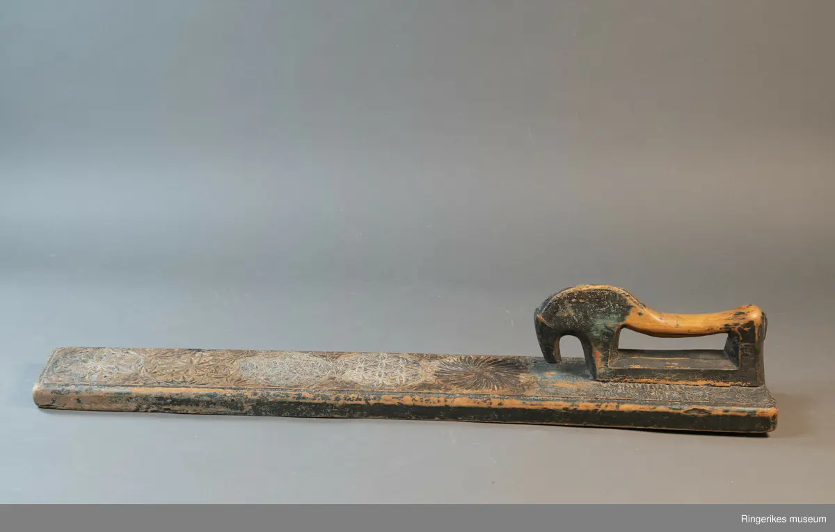 Mangletreet er dekorert med rosetter i mange forskjellige størrelser. Håndtaket er formet som en hest. Hesten har såvidt ører, øyne og munn. Hodet er stort og grovt. Øverst på mangletreet er det festet et oppheng av metall. Det er også rester av et annet oppheng, av strye eller hamp. Hesten er innfelt i mangletreet, resten av mangletreet er laget av massivt tre. Hesten har løsnet fra underlaget, ser ut som om den er festet med en treplugg. Mangletreet er dekorert med rosetter i karveskurd. Nederst er det en kvart rosett i hvert hjørne, med radius på 3 cm. Så kommer en stor rosett med diameter på 9.7 cm. Langs kanten er det to nye halve rosetter på hver side, og en i midten. Den i midten har diameter på 8 cm. De halve har diameter fra 5 cm til 7 cm. (Sett fra hesten: nederst til høyre: 5 cm, øverst til høyre: 6 cm, nederst til venstre: 6 cm, øverst til venstre: 7 cm. Under rosetten i midten står initialene OPD. Deretter kommer en stor rosett, diameter 12.5 cm. Så kommer to små, begge har diameter på 6 cm. Den største rosetten har diameter på 13.5 cm, og er nærmest hesten. Alle unntatt en rosett er dekorert med blomstermotiv. Den ene (halv rosett, øverst til høyre, 5 cm) er dekorert med buede streker. Ellers er det både i og rundt rosettene dekorert med små utskårne trekanter.