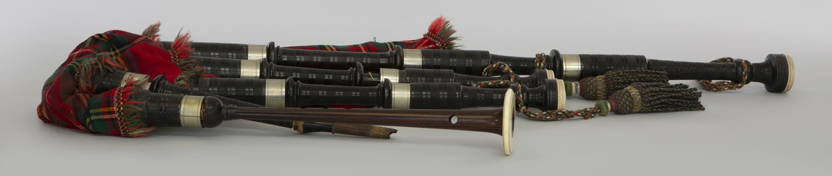 Instrument med vindsekken av skinn, trukket med skotskrutet stoff. Fire piper og ett innblåsningsrør. En skalmeie med syv hull foran og to på sidene. Skalmeien er totalt 45 cm lang og laget av mørkbrunt tre. En bordunpipe 45 cm, den andre 47,5 cm og den tredje 85 cm. Bordunpipene er i ibenholt, riflet på tvers, med sølvringer. Snor med dusk i hver ende er knytet slik at alle pipene er lenket sammen.