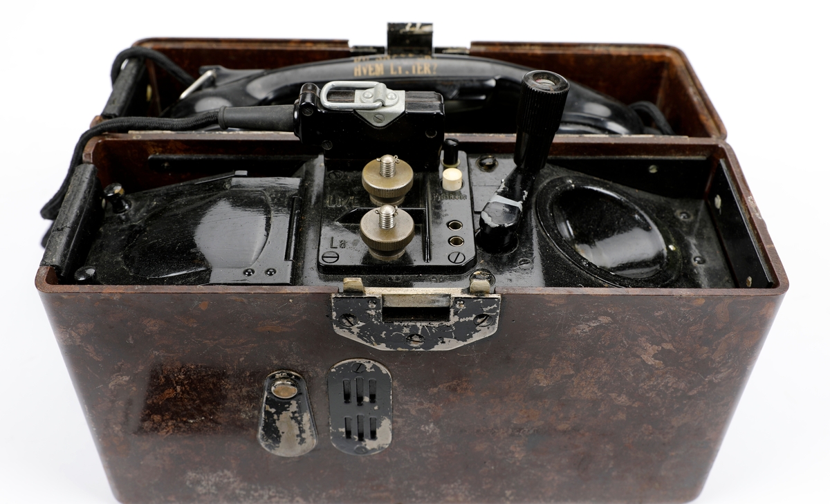 Tyskprodusert felttelefon FF33 (Feldfernsprecher 33). Telefonen er innebygd i en bakelittkasse og mangler bæresele. På lokket er det montert en metallplate med fonetisk alfabet og uttale til ordene og en hvit kodeplate.