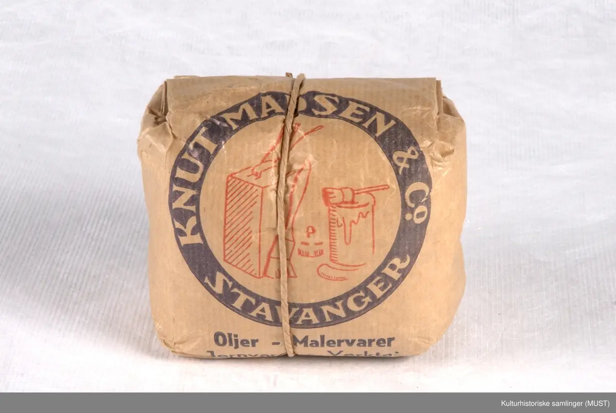 Brun papirpose med blått og rødt trykk. Posen er rullet sammen og holdes lukket med en hyssing som er bundet rundt posen. Kjennes ut som om det er grovt pulver/granulat i posen - antagelig vaskemiddel.