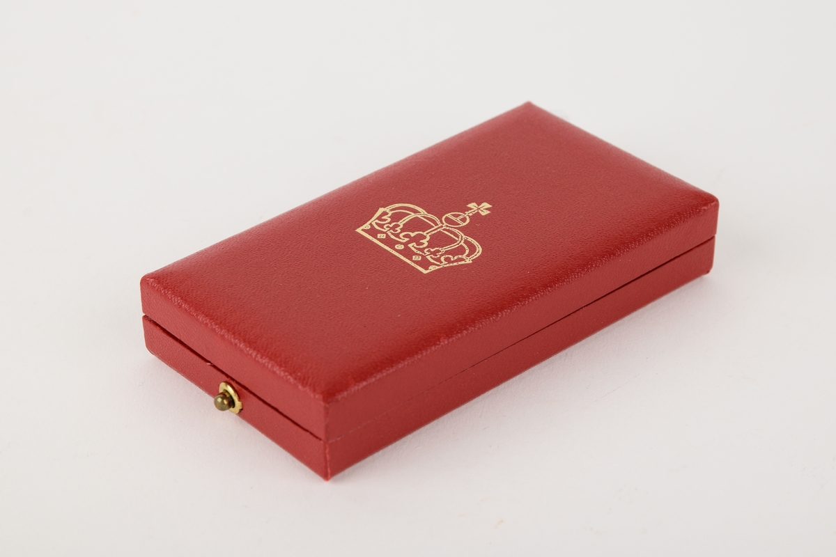 Et eksemplar av "Kongens fortjenstmedalje" i originalt etui. 

Sirkulær medalje med ordensbånd, oppbevart i rektangulært etui. Etuiet har motiv av en krone i sølv på lokket.

