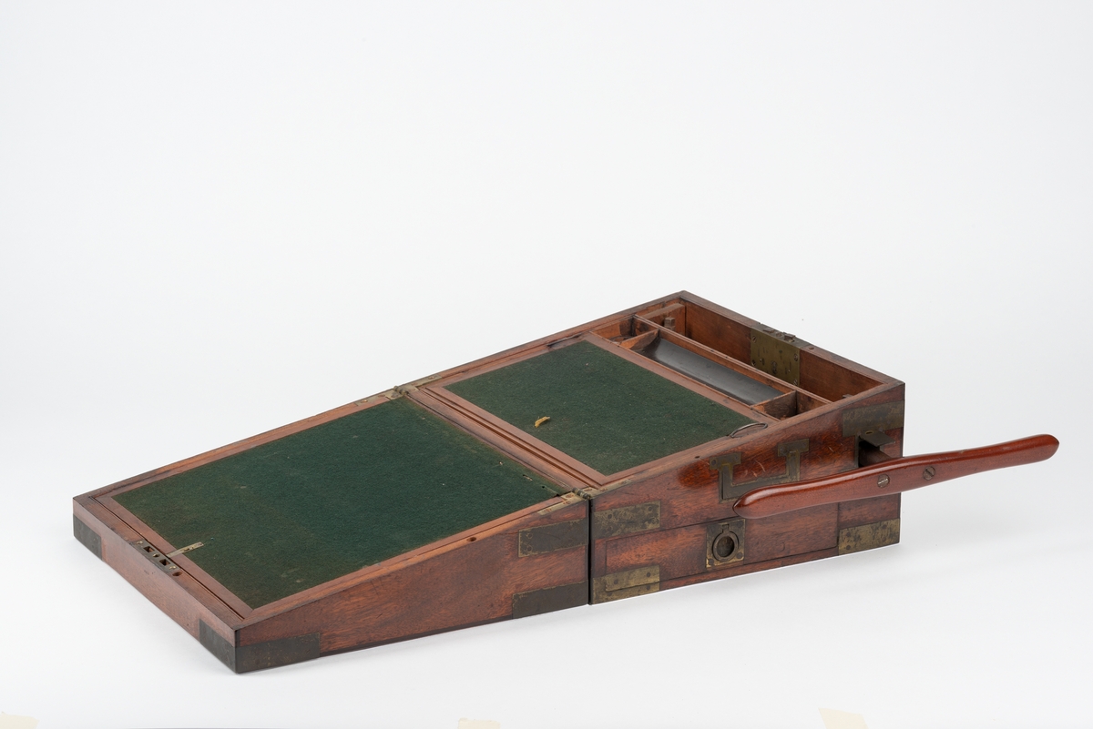 Rektangulær trekasse med kopieringsmaskin. Kassen har flere rom og skuffer. Inni lokket er det et rom som kan åpnes ved å løfte på en klaff. Dette rommet kan være til oppbevaring av papir. Klaffen er foret med filt på den ene siden. Nede i kassa er det en liten, løs trekasse som kan tas ut. I denne er det plass til to blekkhus og pennesplitter. Under den løse trekassen er det et rom med en valse i metall. Valsen kan dreies rundt med en løs sveiv. I bunnen har kassen en uttrekkbar skuff. Kassen har beslag og bærehåndtak i metall. Til kopieringsmaskinen følger det med en løs sveiv, et løst håndtak, et blekkhus og en liten kost.