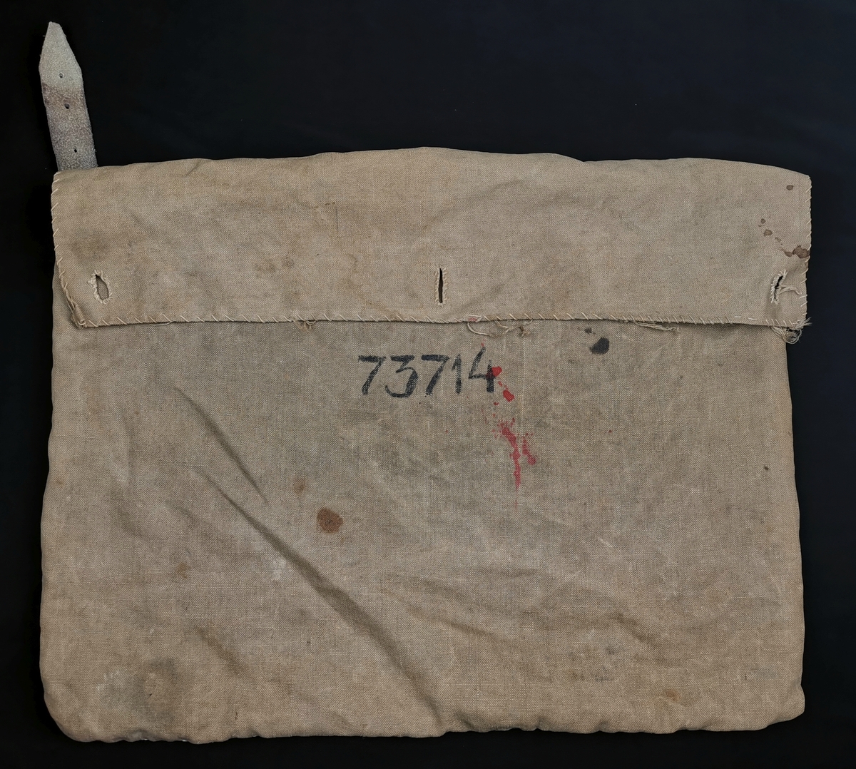 Tøyveske laget av Magdalon B. Andersen under hans fangenskap i Sachsenhausen (1943-45). Veska har en klaff som kan lukkes med tre knapper. På venstreside er påsydd ei lærrem (21 cm). På forsida er fangenummeret fra Sachsenhausen påskrevet. Veska fulgte Magdalon Andersen hele livet, som oppbevaringssted for papirer fra fangenskapet.